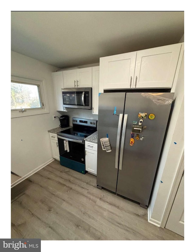 kitchen with white cabinets, light wood-type flooring, stainless steel appliances, and stone countertops