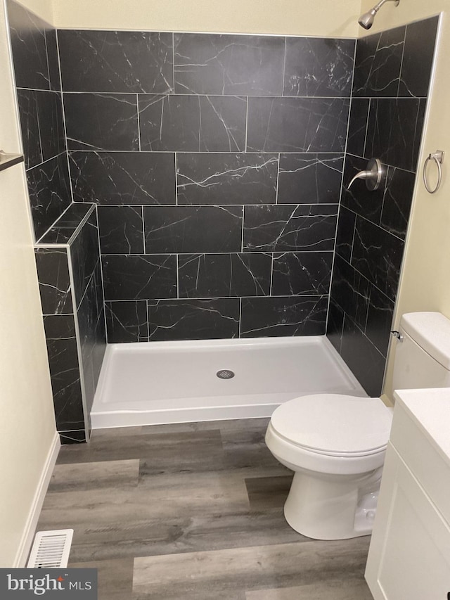 bathroom with a tile shower, vanity, hardwood / wood-style flooring, and toilet