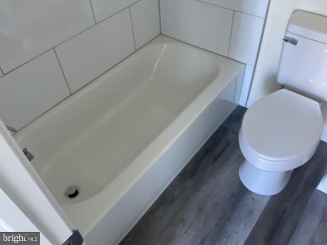 bathroom with hardwood / wood-style flooring, a bathing tub, and toilet