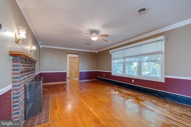 unfurnished living room featuring a fireplace, crown molding, a wood stove, wood-type flooring, and ceiling fan