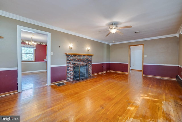 unfurnished living room with crown molding, ceiling fan with notable chandelier, hardwood / wood-style flooring, and a brick fireplace