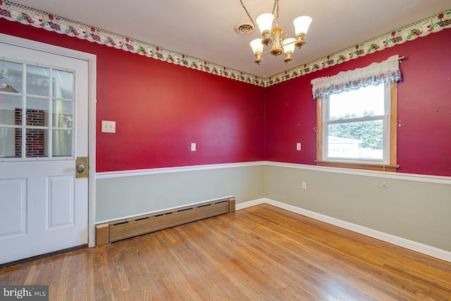 empty room featuring baseboard heating, hardwood / wood-style floors, and a chandelier