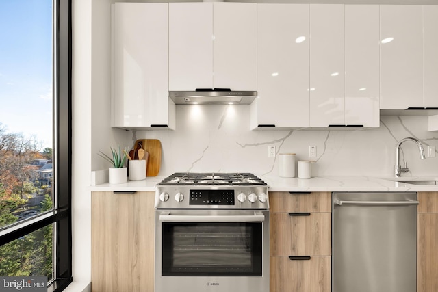 kitchen with modern cabinets, light stone counters, stainless steel appliances, under cabinet range hood, and white cabinetry