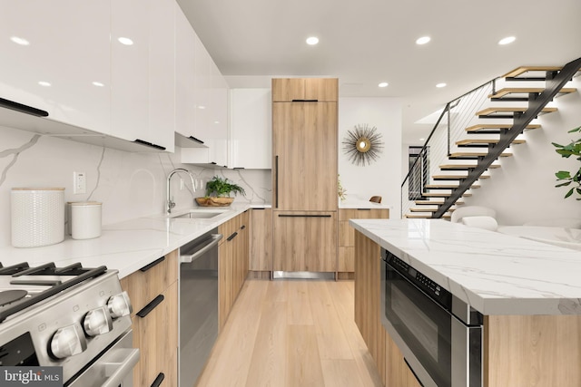 kitchen featuring light stone counters, stainless steel appliances, a sink, white cabinetry, and modern cabinets