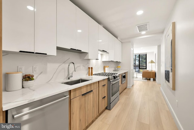 kitchen featuring modern cabinets, appliances with stainless steel finishes, backsplash, and a sink