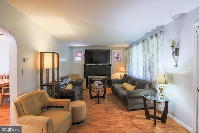 living area with arched walkways, a brick fireplace, wood finished floors, and baseboards