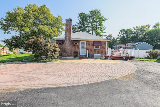 view of front of property with a deck, aphalt driveway, brick siding, fence, and a chimney