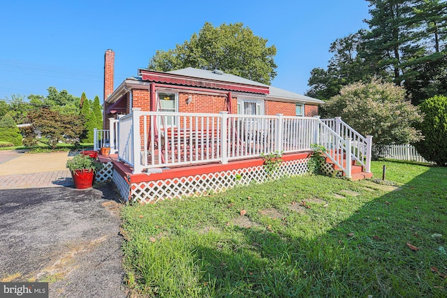 back of house with a deck, brick siding, fence, a yard, and a chimney