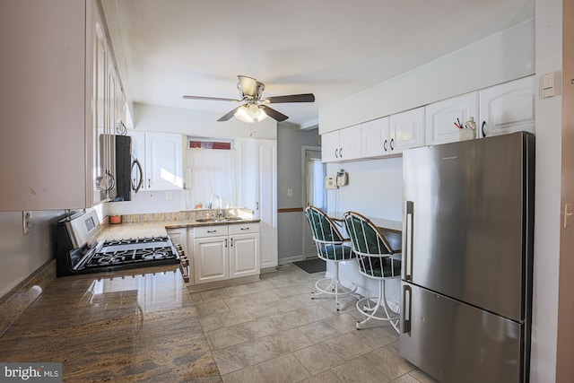 kitchen featuring stainless steel appliances, a sink, white cabinetry, and a ceiling fan