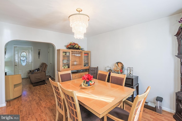 dining room featuring light wood-style floors, baseboards, arched walkways, and an inviting chandelier