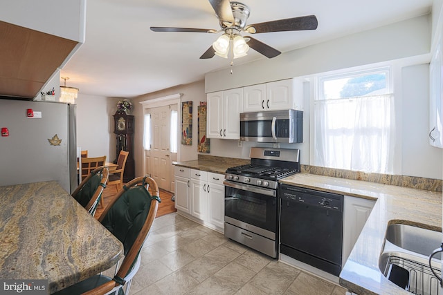 kitchen with ceiling fan, a sink, white cabinets, appliances with stainless steel finishes, and light stone countertops