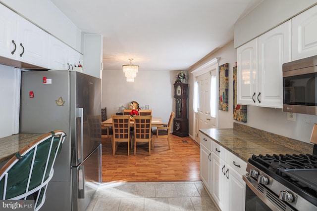 kitchen featuring stainless steel appliances, light wood-style floors, white cabinets, dark countertops, and an inviting chandelier