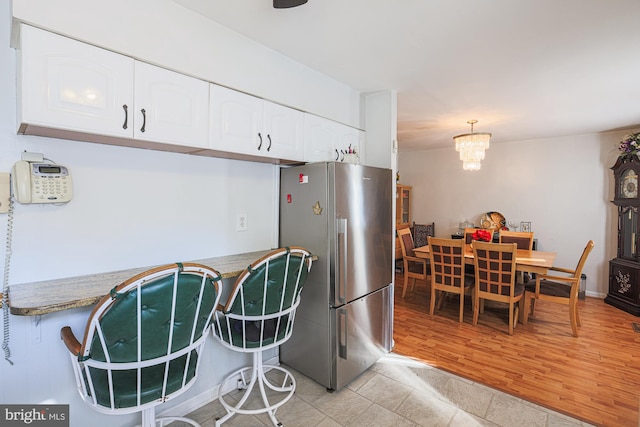 kitchen with decorative light fixtures, freestanding refrigerator, light countertops, light wood-style floors, and white cabinetry