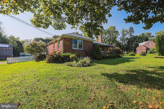 view of property exterior with brick siding, a lawn, a chimney, and fence