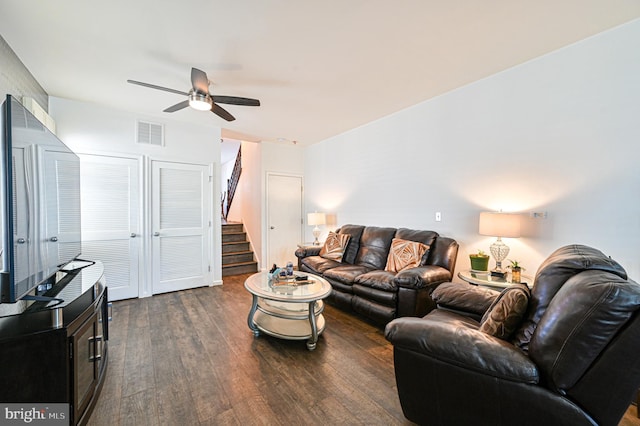 living room with stairway, ceiling fan, visible vents, and dark wood finished floors