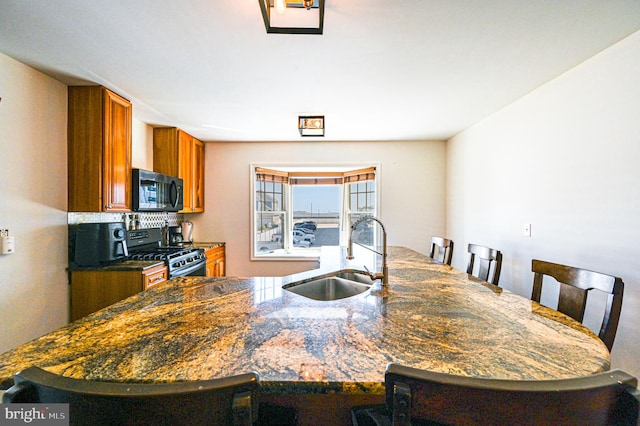 kitchen featuring sink, black appliances, kitchen peninsula, a kitchen bar, and decorative backsplash