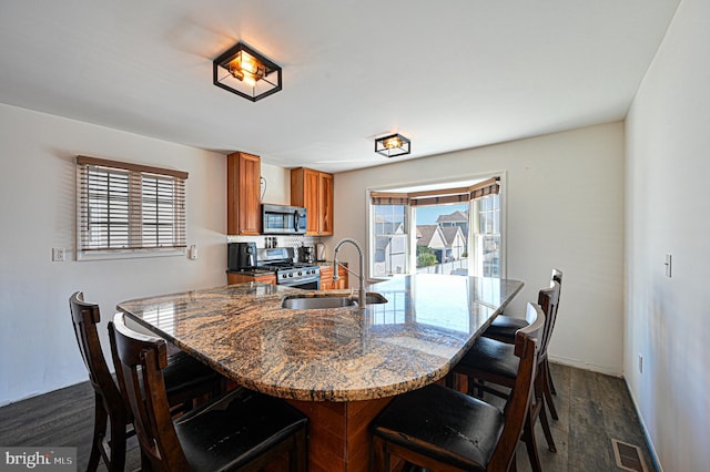 kitchen featuring visible vents, appliances with stainless steel finishes, brown cabinetry, a sink, and a kitchen breakfast bar