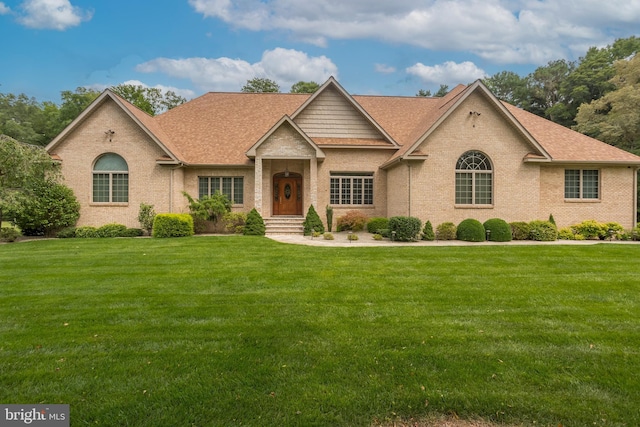 view of front facade featuring brick siding, a front yard, and roof with shingles