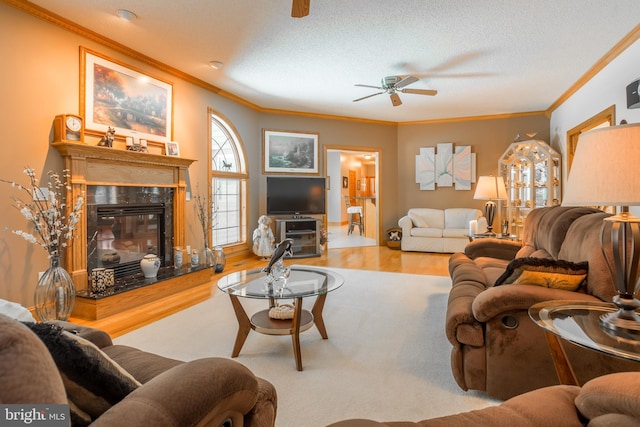 living room featuring light wood-type flooring, ornamental molding, a tile fireplace, and ceiling fan