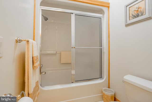 bathroom featuring toilet and shower / bath combination with glass door