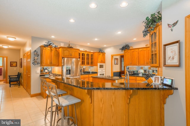 kitchen with brown cabinets, glass insert cabinets, a kitchen bar, white appliances, and a peninsula