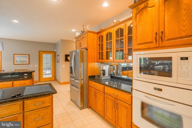 kitchen with a textured ceiling, white appliances, light tile patterned floors, and dark stone counters