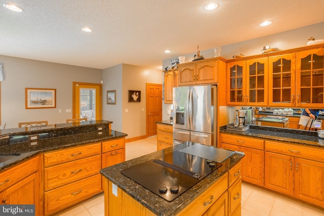 kitchen with a kitchen island, black electric cooktop, stainless steel fridge, glass insert cabinets, and light tile patterned floors