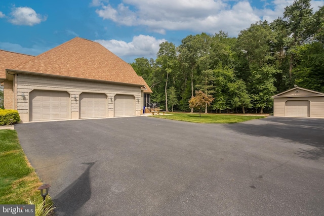 exterior space featuring a shingled roof, an outbuilding, a yard, and a garage