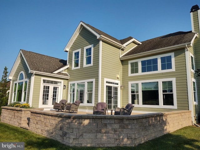 rear view of property featuring a patio area, french doors, roof with shingles, and a chimney