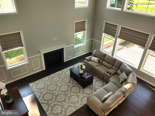 living area with a fireplace with flush hearth, a healthy amount of sunlight, dark wood-style flooring, and a decorative wall