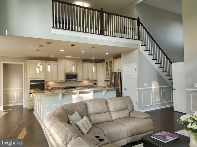 living area featuring a wainscoted wall, dark wood-style floors, stairway, a high ceiling, and a decorative wall