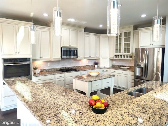 kitchen featuring tasteful backsplash, a center island, light stone countertops, appliances with stainless steel finishes, and a sink