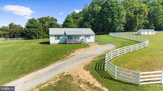 view of front of property featuring a front yard, fence, an outdoor structure, dirt driveway, and metal roof