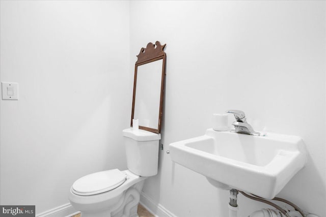 half bathroom featuring toilet, baseboards, and a sink