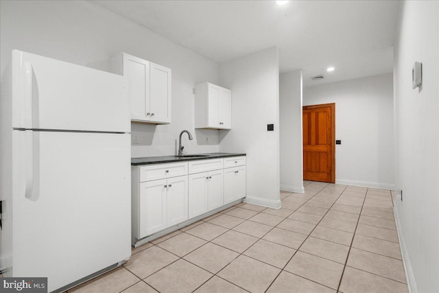 kitchen with light tile patterned flooring, freestanding refrigerator, a sink, white cabinetry, and dark countertops