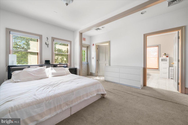 bedroom with visible vents, light colored carpet, and ensuite bath