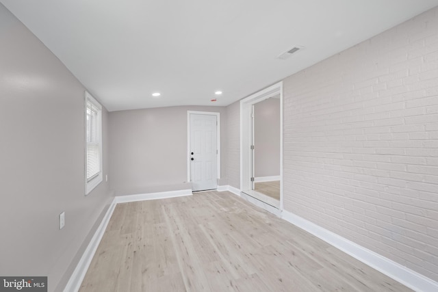 empty room with brick wall and light hardwood / wood-style floors