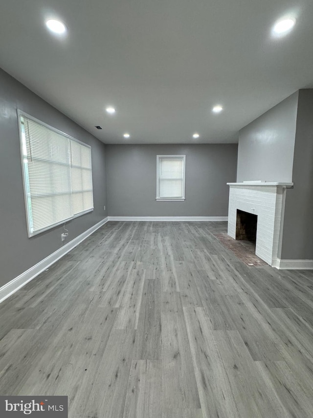 unfurnished living room with wood-type flooring, a wealth of natural light, and a brick fireplace