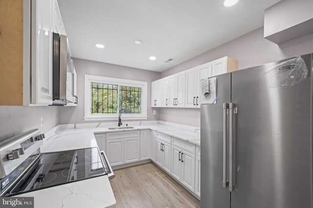 kitchen featuring appliances with stainless steel finishes, white cabinetry, a sink, and light stone counters