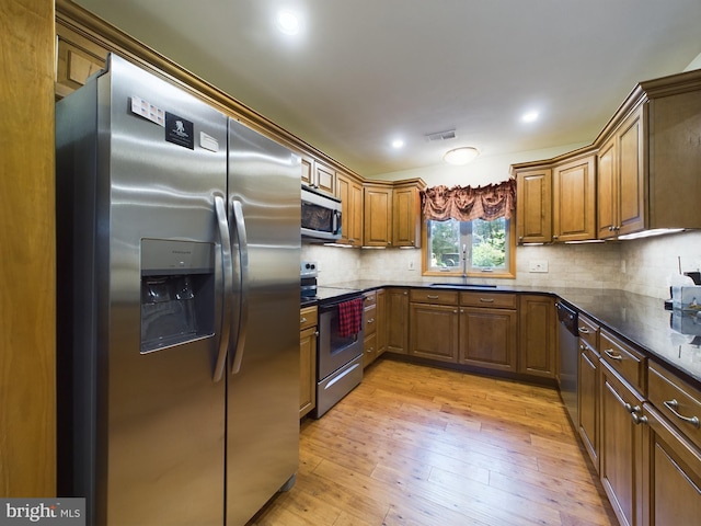 kitchen featuring appliances with stainless steel finishes, sink, tasteful backsplash, and light hardwood / wood-style flooring