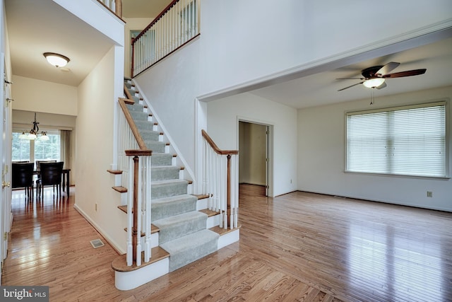 staircase featuring ceiling fan with notable chandelier, hardwood / wood-style floors, and a towering ceiling