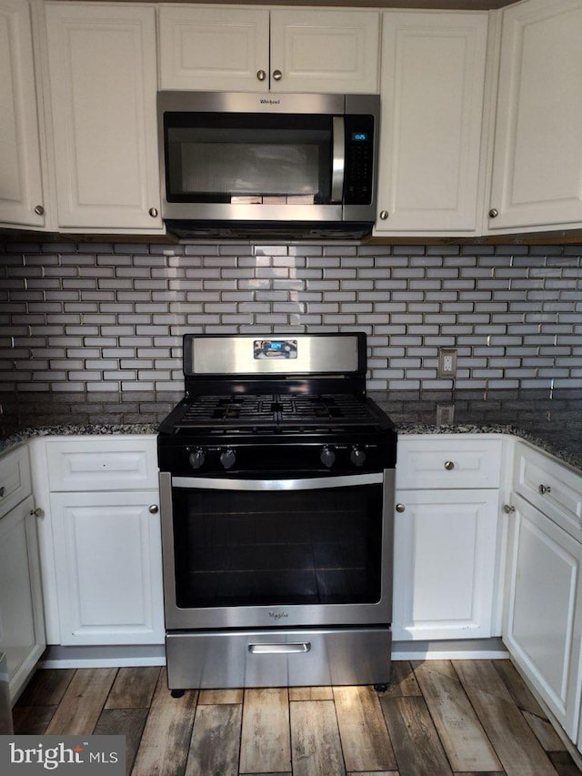 kitchen featuring white cabinets, backsplash, appliances with stainless steel finishes, dark hardwood / wood-style floors, and dark stone countertops