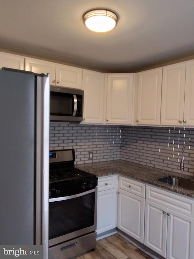 kitchen with appliances with stainless steel finishes, decorative backsplash, white cabinets, light hardwood / wood-style flooring, and sink