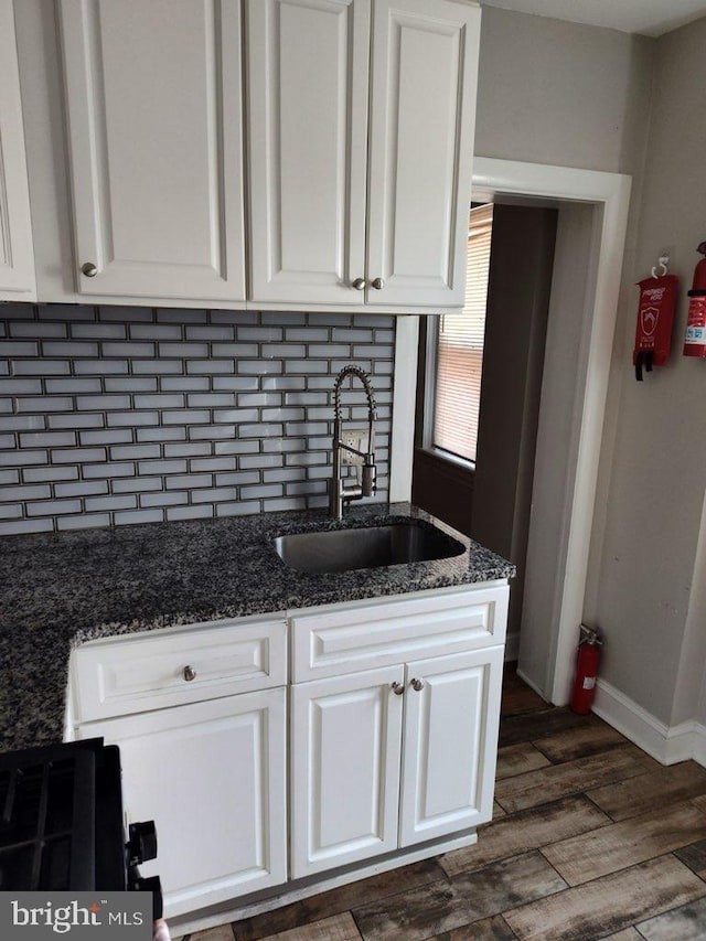 kitchen featuring dark hardwood / wood-style floors, dark stone countertops, white cabinetry, and sink