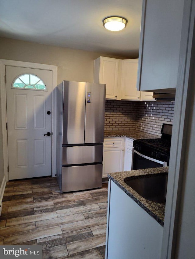 kitchen featuring stainless steel fridge, dark stone countertops, white cabinets, black range with gas cooktop, and hardwood / wood-style floors