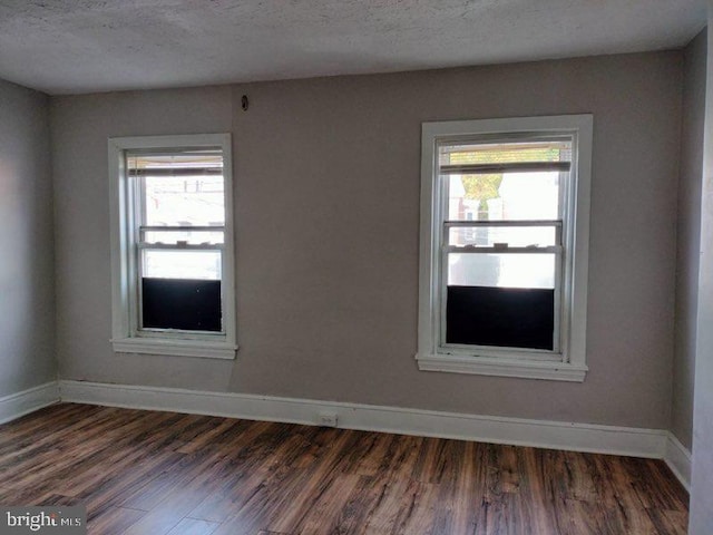 empty room featuring a textured ceiling, plenty of natural light, and dark hardwood / wood-style flooring