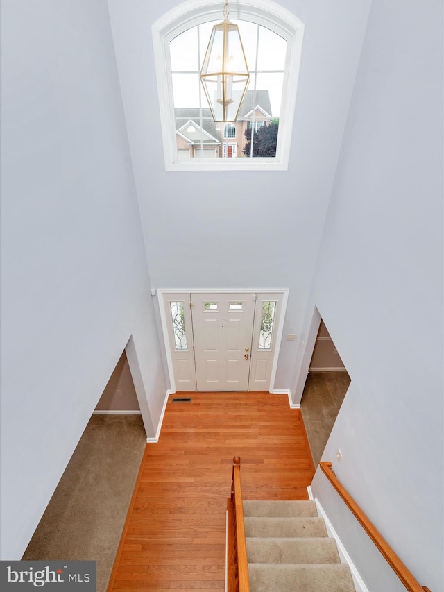 carpeted foyer featuring a towering ceiling, a notable chandelier, and plenty of natural light