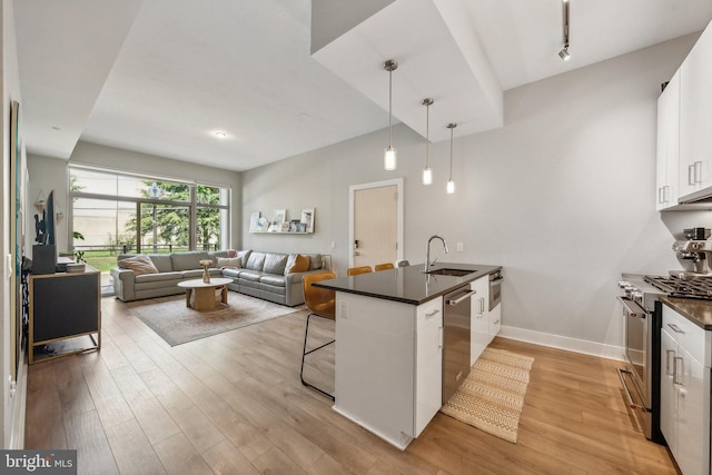 kitchen featuring dark countertops, hanging light fixtures, appliances with stainless steel finishes, open floor plan, and white cabinets