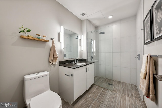 full bathroom featuring toilet, visible vents, tiled shower, and vanity