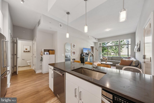 kitchen with white cabinets, dark countertops, appliances with stainless steel finishes, open floor plan, and a sink